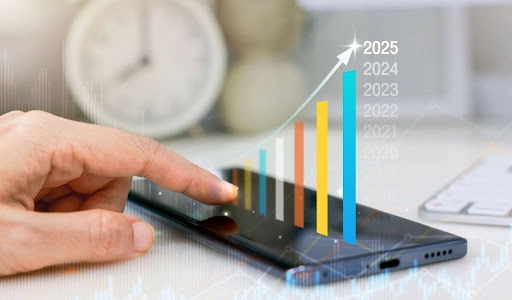 Primer plano de una mano tocando la pantalla de un smartphone donde se proyecta un gráfico de barras ascendentes con años del 2021 al 2025, simbolizando crecimiento financiero
