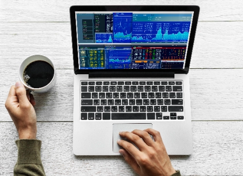 Una vista superior muestra a alguien sosteniendo café mientras opera una computadora portátil con gráficos financieros.