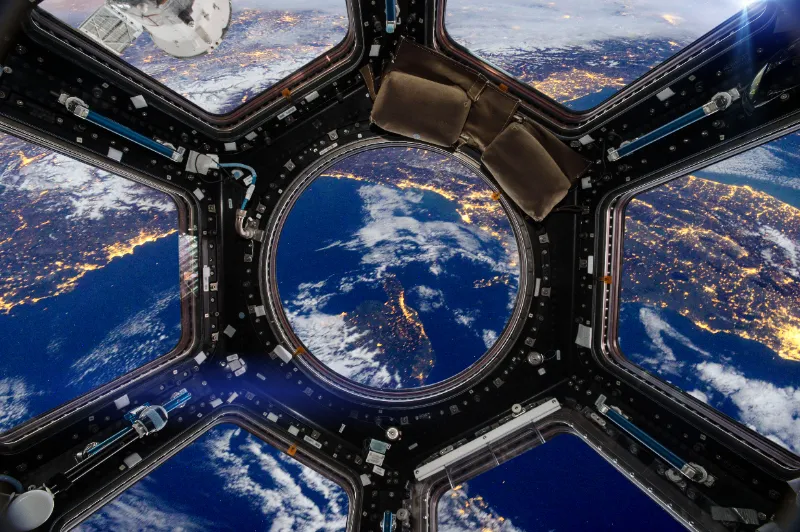 Vista del planeta Tierra iluminado de noche a través de los ventanales de la cúpula de una estación espacial.